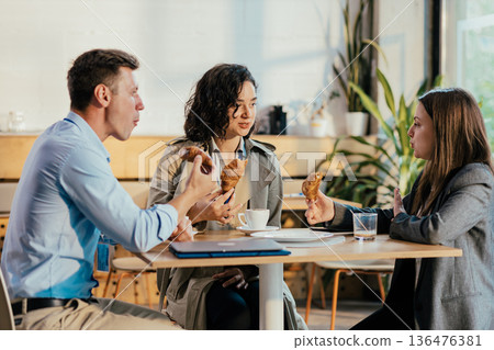 Coworkers enjoying coffee break with croissants and conversation 136476381