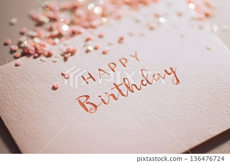 hand-lettered Happy Birthday on pastel card with soft confetti in foreground, soft daylight, shallow depth of field, 136476724