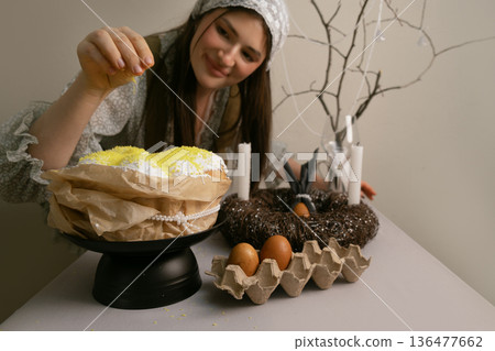 Woman sprinkles coconut on Easter cake at festive table, making final preparations for the Easter celebration. 136477662