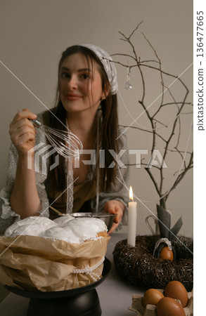 Easter cake comes alive under her care, colorful eggs in a nest and glowing candles nearby, she smiles spreading icing. Easter cake comes alive under her care, colorful eggs in a nest and glowing candles nearby, she smiles spreading icing. 136477665