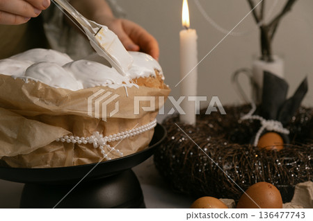 In cozy kitchen, she spreads icing on Easter cake, with eggs, candles, twig wreath on table, and beaded branch in background. In cozy kitchen, she spreads icing on Easter cake, with eggs, candles, twig wreath on table, and beaded branch in background. 136477743
