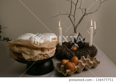 Cozy home Easter scene with cake in white icing, eggs in tray, candles, and decorative twig nest on the table. Cozy home Easter scene with cake in white icing, eggs in tray, candles, and decorative twig nest on the table. 136477751