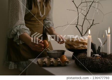 She carefully arranges treats and candles for Easter, immersed in a warm and caring home atmosphere. She carefully arranges treats and candles for Easter, immersed in a warm and caring home atmosphere. 136477760