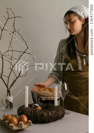 Woman in home clothes with headscarf and apron preparing Easter table, filling the home with warmth and joy. 136477866