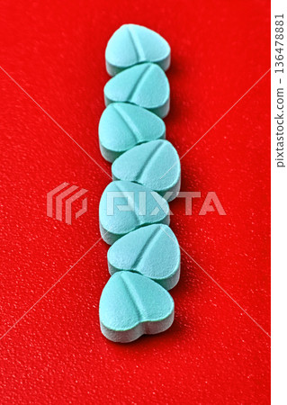 Blue heart-shaped cardiology pills lined up on a red background. Blue heart-shaped cardiology pills lined up on a red background. 136478881