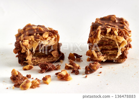 Close-up of a broken chocolate caramel bar with nuts on a white background. Close-up of a broken chocolate caramel bar with nuts on a white background. 136478883