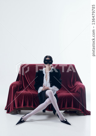 Woman wearing black mask sitting on red velvet sofa in poetcore style. 136479785
