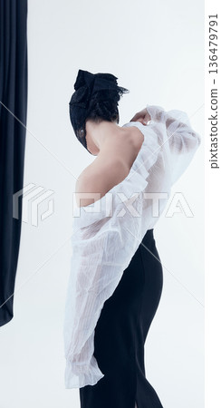 Woman in romantic poetcore outfit adjusting sheer ruffled blouse in bright white studio 136479791