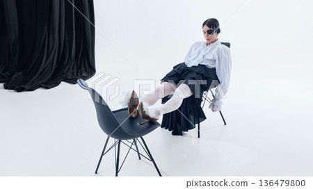 Woman with dark eye patch reclining on chair in layered black skirt Woman with dark eye patch reclining on chair in layered black skirt 136479800