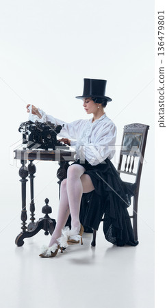 Poetcore muse in top hat working on vintage typewriter in bright studio. 136479801