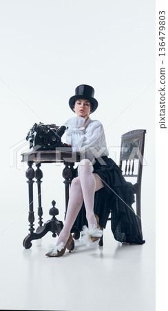 Woman in top hat sitting at antique desk with typewriter in poetcore style. 136479803