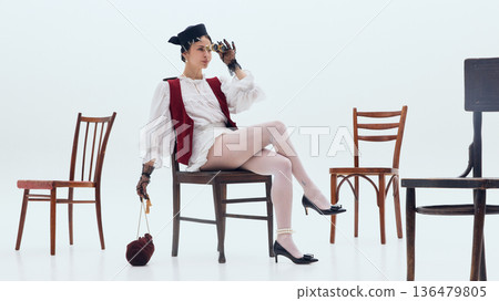 Stylish woman seated with vintage binoculars in minimalist white space. 136479805
