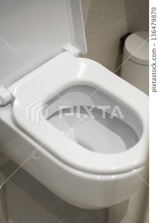 White ceramic toilet in a modern bathroom, seat cover open, representing concepts of hygiene, plumbing, sanitation, design, cleanliness, and residential decor 136479870