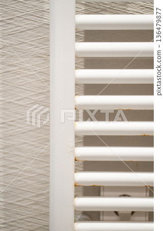 White bathroom towel rail radiator showing signs of rust and corrosion, indicating metal degradation and the need for home maintenance or a plumbing repair White bathroom towel rail radiator showing signs of rust and corrosion, indicating metal degradation and the need for home maintenance or a plumbing repair 136479877