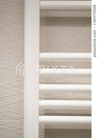 White towel radiator installed on a textured light beige wall in a modern bathroom, providing warmth and a practical drying solution White towel radiator installed on a textured light beige wall in a modern bathroom, providing warmth and a practical drying solution 136479886