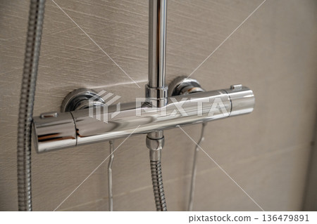 Chrome thermostatic shower mixer tap with flexible hose on light grey tiled wall, providing modern bathroom functionality and water temperature control 136479891