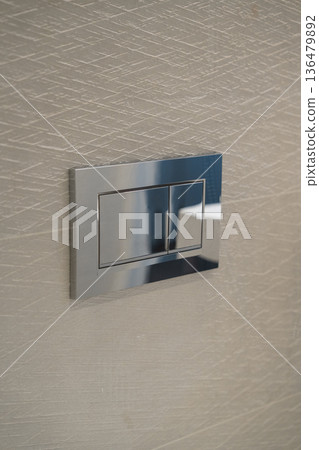 Chrome dual flush plate mounted on a stylish textured wall, representing modern bathroom design, efficient water usage, and contemporary home interior finishes Chrome dual flush plate mounted on a stylish textured wall, representing modern bathroom design, efficient water usage, and contemporary home interior finishes 136479892