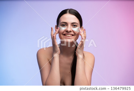 Young woman applying nourishing under-eye patches, engaging in daily skincare and self-care routine, promoting beauty, hydration, and healthy glowing skin 136479925
