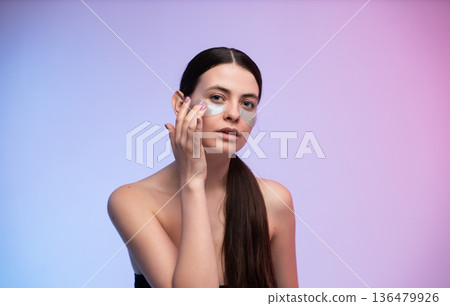 Woman standing topless, applying hydrating collagen eye patches with her finger, taking care of her face with a rejuvenating treatment, promoting beauty and skincare Woman standing topless, applying hydrating collagen eye patches with her finger, taking care of her face with a rejuvenating treatment, promoting beauty and skincare 136479926