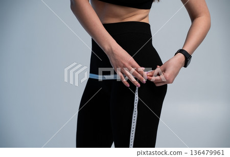 Woman measuring hips with a tape measure, monitoring weight loss progress and body transformation, focusing on fitness, healthy lifestyle, and diet goals Woman measuring hips with a tape measure, monitoring weight loss progress and body transformation, focusing on fitness, healthy lifestyle, and diet goals 136479961