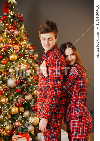 Couple in red pajamas by Christmas tree at home Couple in red pajamas by Christmas tree at home 136480416