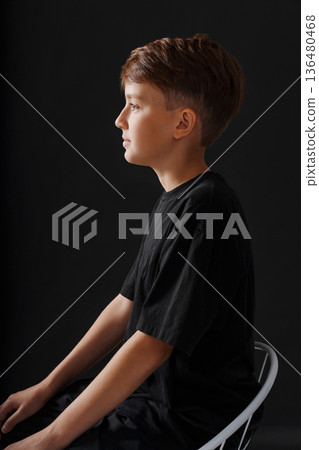 Young boy sitting in profile view against a dark background Young boy sitting in profile view against a dark background 136480468