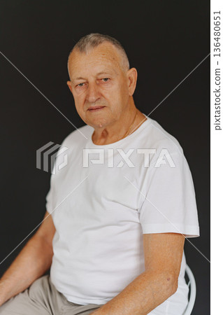 Older man sitting on chair with simple background and calm expression 136480651