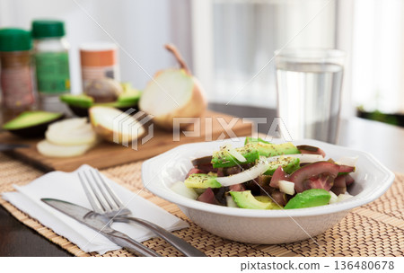 salad of black tomatoes, avocado and onions in white ceramic bowl 136480678