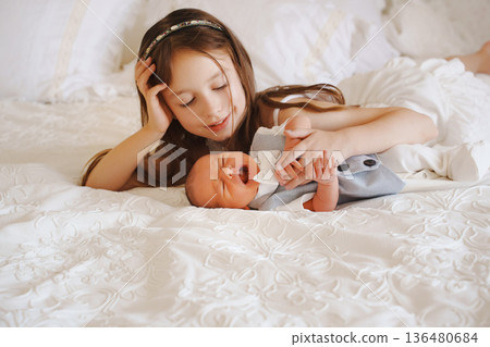 Sister plays with newborn brother on bed in cozy room Sister plays with newborn brother on bed in cozy room 136480684