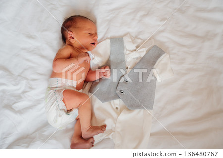 Baby lays next to gray vest and shirt on white cloth Baby lays next to gray vest and shirt on white cloth 136480767
