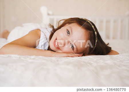 Girl smiles while lying on a bed in a bright room Girl smiles while lying on a bed in a bright room 136480770