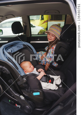 Child sits next to baby in car seat during family trip 136480781