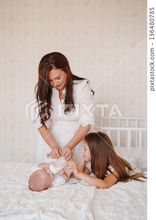 Mom caring for baby while sister watches lovingly Mom caring for baby while sister watches lovingly 136480785