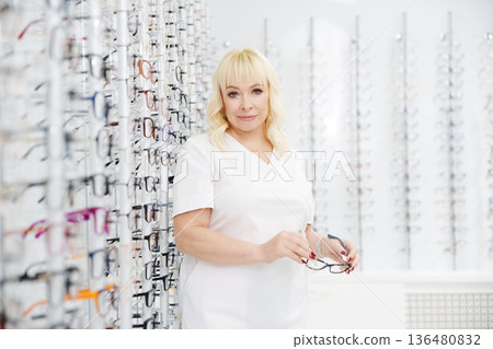 Ophthalmologist standing in optical store with glasses Ophthalmologist standing in optical store with glasses 136480832