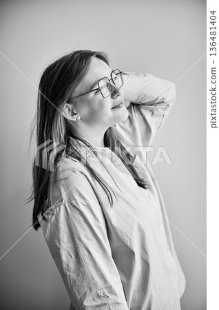 Side view of young female happily smiling and looking away. Portrait of lovely girl in cream shirt standing in natural light. Black and white image. 136481404