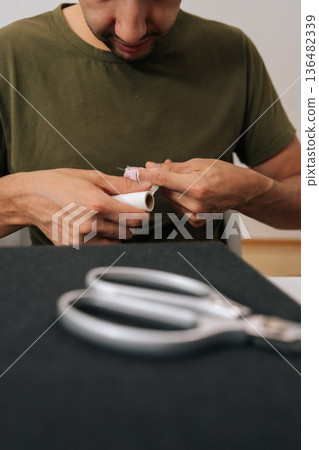 Vertical shot of young man applying medical patch to injured finger, demonstrating self-care for minor hand wound at home, preventing infection and managing discomfort after accident. Vertical shot of young man applying medical patch to injured finger, demonstrating self-care for minor hand wound at home, preventing infection and managing discomfort after accident. 136482339