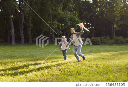 Happy father and child running in park, flying colorful kite and enjoying fun outdoor time together. Happy father and child running in park, flying colorful kite and enjoying fun outdoor time together. 136483105