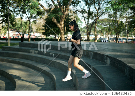 Female runner jogging down concrete steps during outdoor workout in urban park with morning light Female runner jogging down concrete steps during outdoor workout in urban park with morning light 136483485