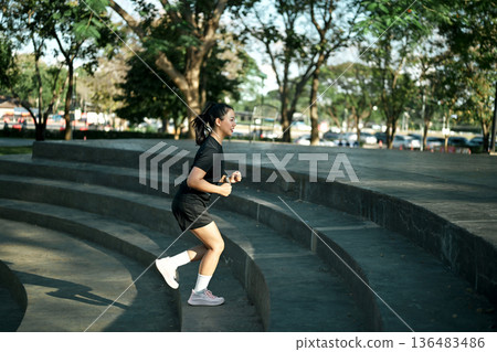 Female runner jogging down concrete steps during outdoor workout in urban park with morning light Female runner jogging down concrete steps during outdoor workout in urban park with morning light 136483486