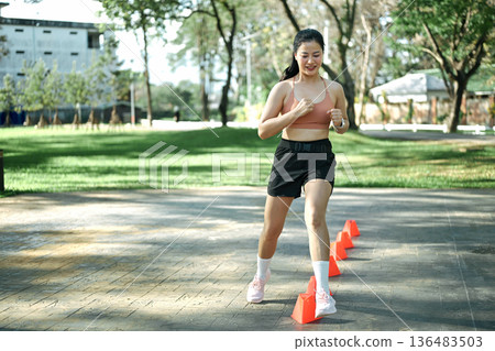Woman doing speed and agility cone drills workout session outdoors 136483503