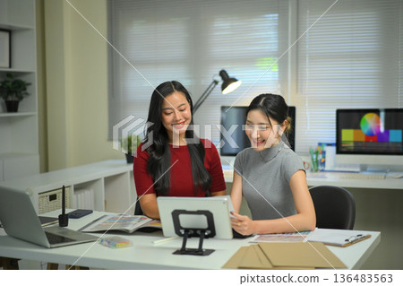 Young women discussing graphic design work at office desk, creative teamwork, planning ideas and modern workplace collaboration. 136483563