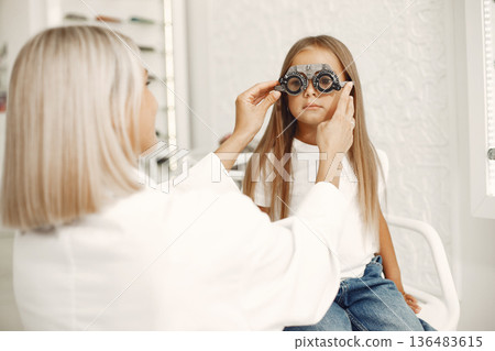 Child eye test and eye exam. Little girl having eye check-up, with phoropter. Doctor performs eye test for child. 136483615