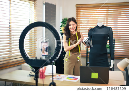 Young influencer woman blogger showing dress in front of smartphone camera while recording or live streaming at home Young influencer woman blogger showing dress in front of smartphone camera while recording or live streaming at home 136483809