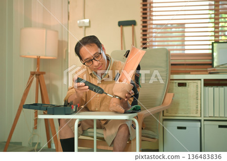 Middle aged man repairing a prosthetic leg at home with a screwdriver, focused self care and independence during disability adaptation 136483836