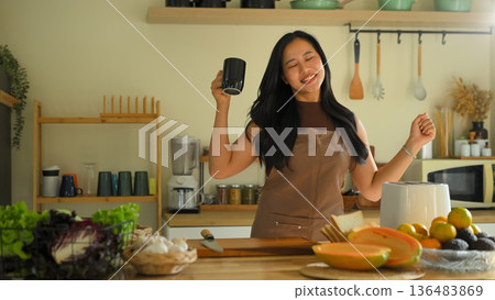 Happy woman dancing while preparing healthy breakfast in a cozy kitchen, enjoying morning routine Happy woman dancing while preparing healthy breakfast in a cozy kitchen, enjoying morning routine 136483869