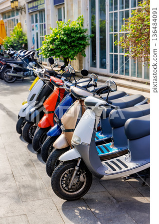Colorful Row of Modern Scooters Parked on Sidewalk 136484091