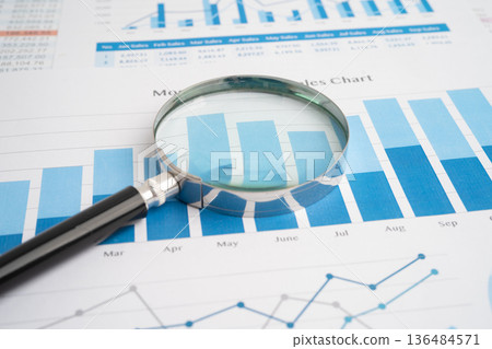 Magnifying glass on spreadsheet and graph paper. 136484571