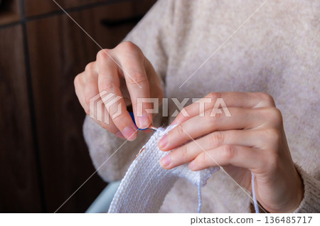 A close-up of a young Caucasian woman's hands crocheting a woolen item at home. A pleasant, meditative hobby. 136485717