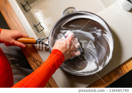 A close-up with localized lighting. The hands of a Caucasian woman washing dishes in a home kitchen late at night in the dark. 136485740