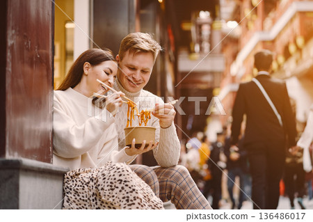 newlywed couple eating noodles with chopsticks in Shanghai outside a food market near Yuyuan. Couple eating authentic local food. husband and wife eating chinese food outisde of a food hall newlywed couple eating noodles with chopsticks in Shanghai outside a food market near Yuyuan. Couple eating authentic local food. husband and wife eating chinese food outisde of a food hall 136486017